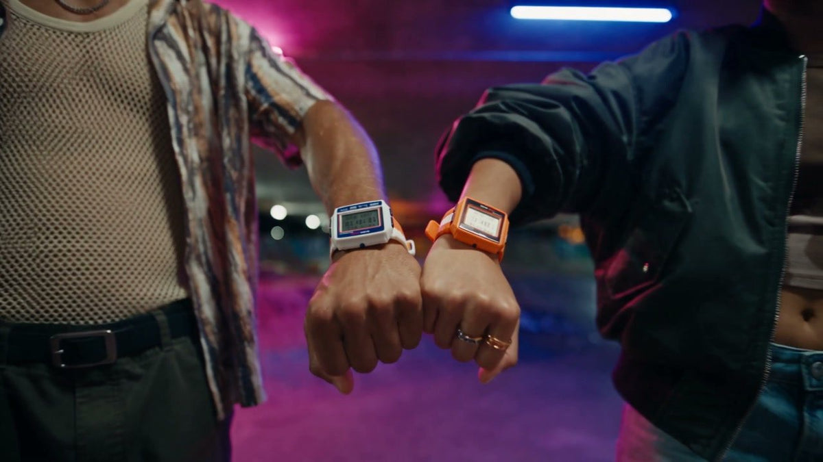Orange and Blue RetroWave calculator watches worn side by side under neon light
