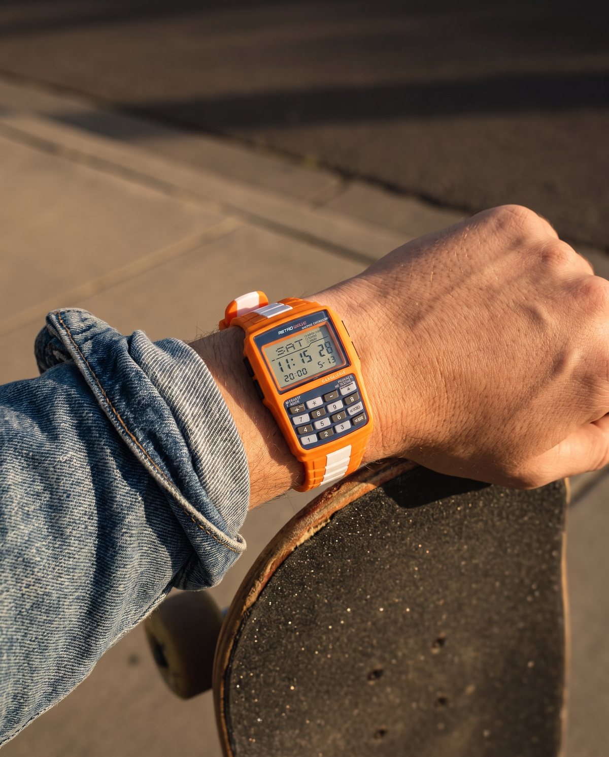 Orange RetroWave calculator watch worn on a wrist resting on a skateboard