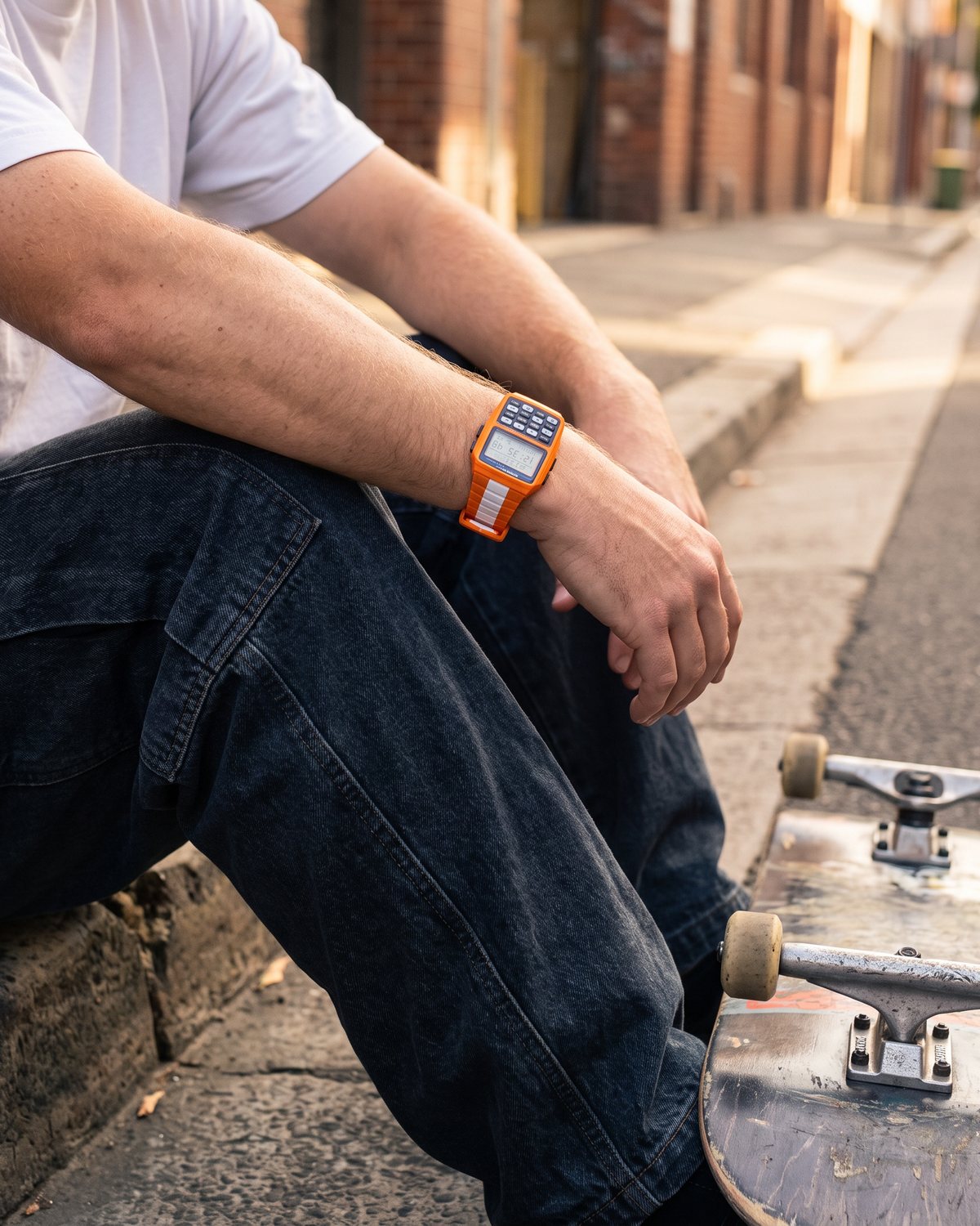 Skater sitting on a kerb wearing the Orange RetroWave calculator watch